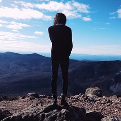 Rear view of woman standing on rock by mountains against sky