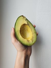 Close-up of hand holding fruit against white wall