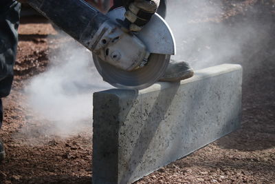 Low section of manual worker cutting stone on field