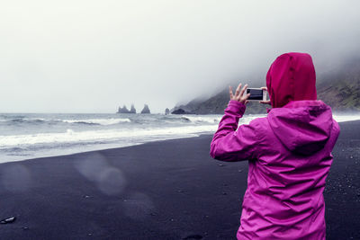 Rear view of person photographing sea against sky