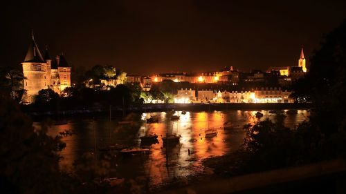 Illuminated buildings by river against sky at night