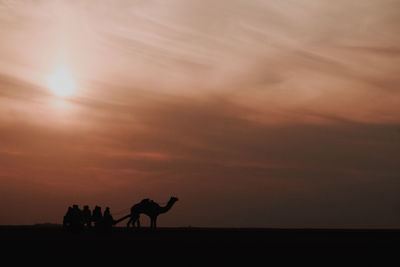 Silhouette people riding horse on beach against sky during sunset