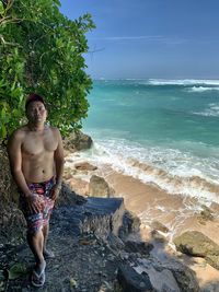 Full length of shirtless man standing at beach against sky