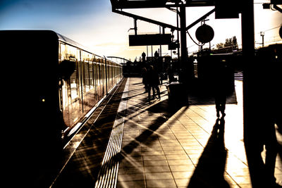 Silhouette people walking on railroad tracks against sky during sunset