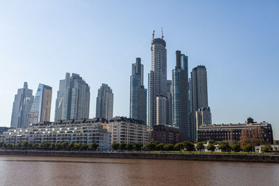 Modern buildings by river against sky in city