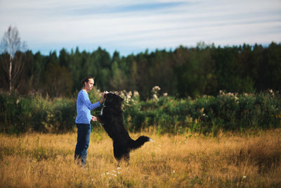 Side view of man playing with dog on grassy land