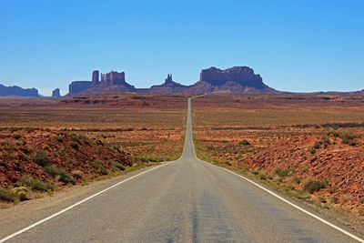 Road leading towards mountain against blue sky