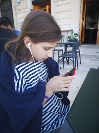 A girl in a towel and a striped dress at a table in a street cafe listening to music  her smartphone
