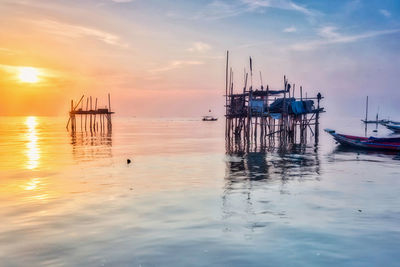 Sailboats moored in sea against sky during sunset