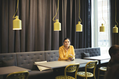 Mid adult businesswoman with book sitting at table in cafeteria at office