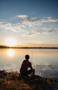 Adolescent boy fishing on shore of lake at sunset in ontario, canada.