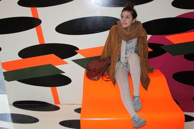 Portrait of young woman standing against orange wall