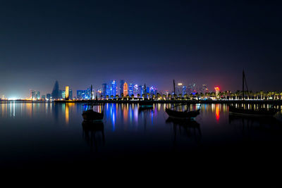 Coloful illuminated skyline of doha, qatar  at night with wooden boats called dhows against dark sky