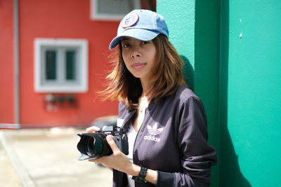 Portrait of woman with camera looking away against wall