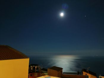 Illuminated buildings by sea against sky at night