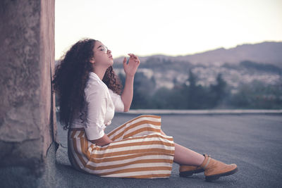 Young woman with curly hair looking away while sitting outdoors 