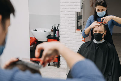 Female barber wearing mask cutting hair of man at salon