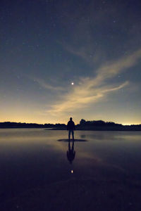 Silhouette man standing amidst lake against dusk