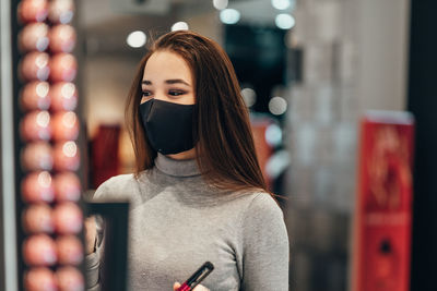 Smiling young woman wearing mask shopping at cosmetic store