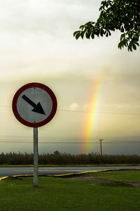 Road sign on field against sky during sunset