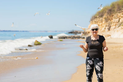 Elderly woman in dark sunglasses feeds seagulls on the beach