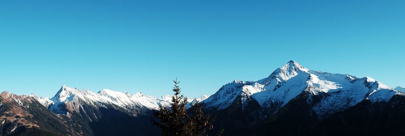 Low angle view of snowcapped mountains against clear blue sky