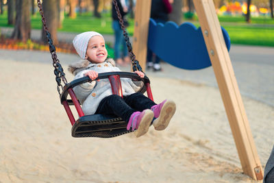 Cheerful cute girl sitting on swing at playground