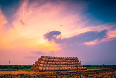 Stack of hay bales on field against sky during sunset
