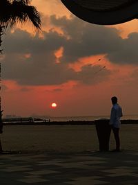 Silhouette man standing on beach against sky during sunset