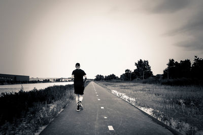 Rear view of man jogging on road against clear sky