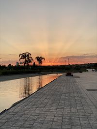 Footpath by swimming pool against sky during sunset