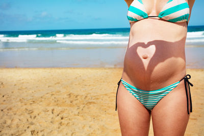 Midsection of woman in bikini at beach