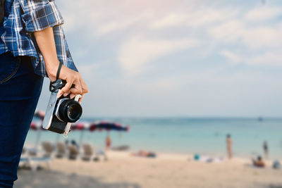 Midsection of woman holding camera on beach