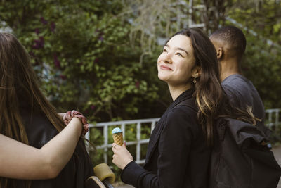 Smiling young woman holding ice cream while walking with friends