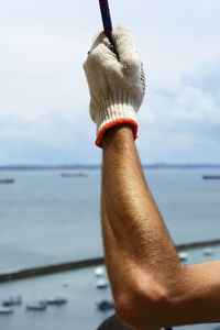 Close-up of hand with glove holding a rope against the sky.