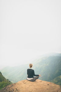 Rear view of woman doing yoga on rock against mountain