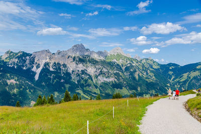 Rear view of people walking on road towards mountains against sky