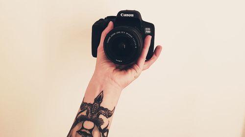 Close-up of hand holding camera against white background