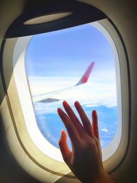 Cropped image of woman hand against sky seen through airplane window