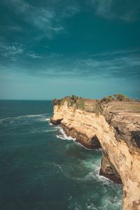 Rock formation by sea against blue sky