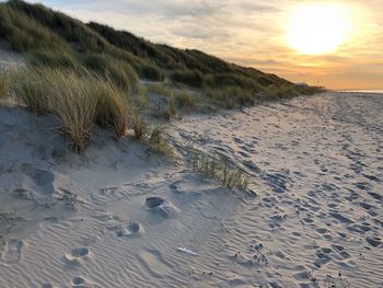 Footprints on sand at beach against sky during sunset