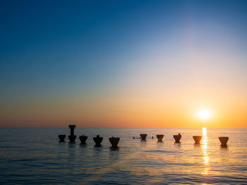 Silhouette people swimming in sea against sky during sunset