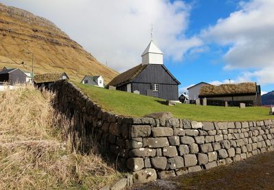 Stone wall of building on field against sky