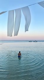 Rear view of man in sea against sky during sunset