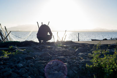 Rear view of person on rock at beach against sky