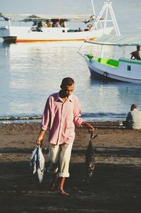 Full length of man holding fish while walking against sea