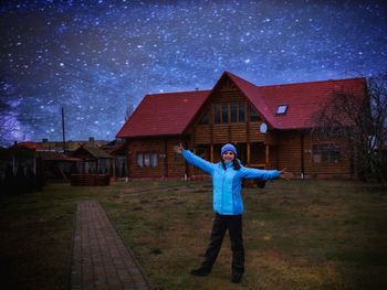 Portrait of teenage girl standing with arms outstretched against house at night