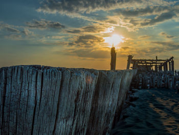 Wooden post in sea against sky during sunset