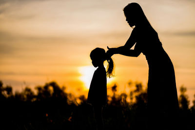 Silhouette of mother and daughter on field at sunset