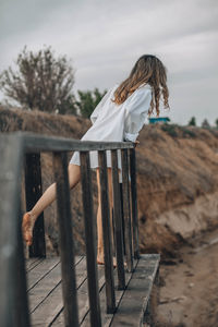 Unrecognizable woman in white shirt on wood platform, back view, personal reflection, nature retreat